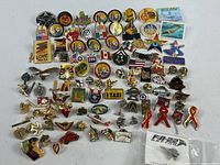 Full view of about 70 assorted pins laid out on a white surface, showing a wide variety of designs involving flags, logos, cartoon characters, symbols, and awareness ribbons.