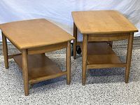 Both side tables shown together. Each has a drawer and an underside shelf. Rectangular tops with rounded corners and tapered legs.