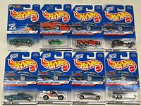 Front view of eight Mattel Hot Wheels 1998 First Editions cars in original sealed blue blister cards. Cars are various colors including green, red, orange, silver, and white. Packaging clearly states "1998 First Editions".