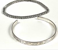 Two bracelets displayed: one silver tennis bracelet with clear stones and one silver cuff bracelet with engraved inspirational words and heart designs.