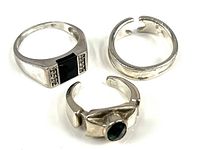 Group photo showing three sterling silver rings: one with a dark rectangular stone and clear stones, one plain adjustable band, and one adjustable ring with a green oval stone.