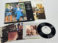 Photo showing four 45 RPM singles by various artists including Madonna and Big Oil, displayed with the vinyl disc visible for one single.