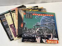 Stack of nine vintage rock vinyl albums, identifiable covers include REO Speedwagon's "Wheels Are Turnin'" and others behind it.