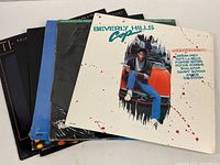 Photo showing stacked vinyl albums with Beverly Hills Cop album prominently on top, followed by others in partially visible covers.