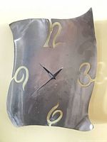 Front view of brushed steel wall clock showing cut-out numerals and hands
