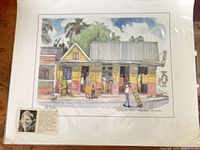 Print showing colourful shop with people in front, signature visible