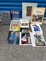 Photo showing all 11 art books and prints arranged on the ground in front of a blue background.