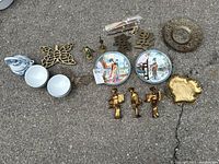 Overall set laid out on the ground showing decorative plates, brass butterfly, statues, teapot, bowls, and other brass items.