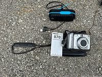 Photo of Canon PowerShot A720 IS camera, black carrying case, and portable speaker on asphalt surface with MaxSold tag.