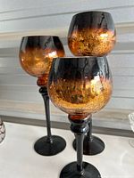 Three matching amber and gold colored glass candle holders with black stems and bases, shown together to highlight size variation and design.