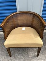 Front view of the armchair showing woven cane back, wooden frame, and beige cushioned seat.