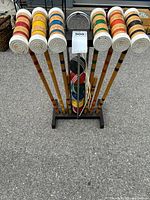 Front view of croquet set with 6 mallets arranged upright on black metal stand, colorful balls in center.