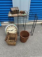Full lot arranged outside showing wicker top table, pirate chest, sewing box, clock, baskets, wrought iron shelf.