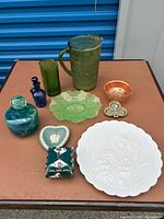 Overview of all decorative glass and ceramic items laid out on a brown surface, showing various bottles, dishes, bowls, and pitcher.
