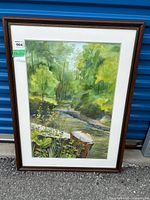Framed watercolor painting showing a forest stream with greenery and tree stump in front, signed S. Kingdom.