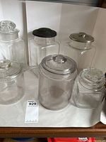 Front view of six glass jars with various lids on a white backdrop showing condition and wear.