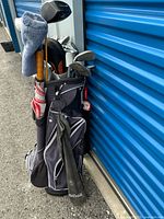 Golf bag filled with various golf clubs, umbrella, and other accessories shown from the front and side outside a blue storage unit.