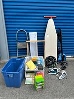 Full lot of laundry and cleaning items visible: ironing board, step ladder, irons, drying rack, vacuum, and blue bin