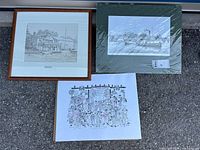 Three prints displayed outside: one wood framed black and white Oakville Club print, one green matte wrapped Windemere print, and one colorful unframed print.