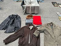 Four men's coats arranged on the floor showing the Danier and Wilson leather jackets, trench coat, and accessories including two scarves and a fur-like hat.