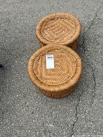 Two round woven foot stools placed on asphalt surface, showing top pattern and size.