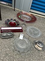 Overview of assortment showing glass platters, metal serving pieces, Mikasa cake cutter in case, small decorative plate, and truffle bowl.