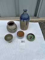 Five pottery pieces arranged on white surface showing variety of shapes and glaze colors.