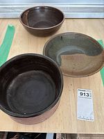 Three ceramic pottery bowls on a wood surface with a MaxSold tag nearby
