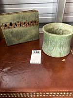 Photo showing both ceramic items together on a brown surface, the square vase with cutout design next to round planter