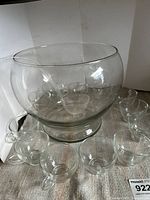 Main photo showing large clear glass punchbowl, clear plastic ladle inside, and arranged 12 clear glass cups around it.