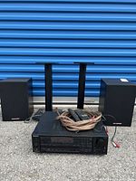 Sony STR-AV720 stereo receiver with speaker cables and two remote controls on top, two Carvin Vegal speakers behind, and two speaker stands further behind.