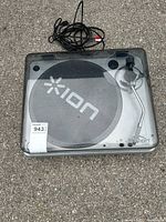 Ion USB Turntable closed with power cord visible on top, dark transparent dust cover, silver base with Ion logo on the mat.