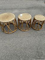 View of all three wicker nesting tables in graduated sizes arranged side by side on pavement, showing their round woven tops and open base structure.