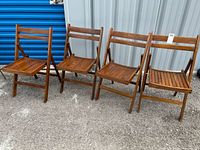 Four wooden folding chairs arranged side by side, showing front and side views with visible wear on wood surfaces.