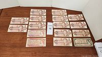 Overview of all 16 Canadian 2 dollar bills laid out on a wooden surface.