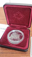 Silver coin inside open black case lined with red velvet featuring an embossed maple leaf on the lid.