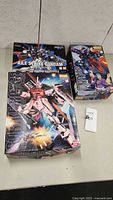 Three boxed Ban Dai Gundam model kits: Aile Strike Gundam (1:144), Master Gundam Neo Hong Kong (1:100), Strike Rouge Orb (1:100) arranged on a table