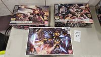 Three Bandai HG model kit boxes with assembled model figures present on a table
