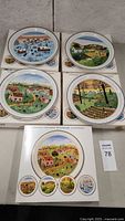 Full set of five plates laid out on original boxes showing village seasonal scenes with naive art style