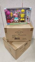Boxed Peppa Pig 12-piece play set showing Peppa figure in white dress and accompanying figure in yellow raincoat with black boots, displayed on two shipping boxes.