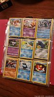 Red binder open showing 9 Pokemon cards in clear sleeves, cards include Water-type and Psychic-type with bending/warping