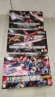 Three boxed Bandai Gundam model kits stacked, showing Gunner Zaku Warrior, Sword Impulse Gundam, and RX-0 Unicorn Gundam 02 Banshee Destroy Mode.