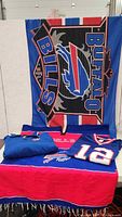 Full lot displayed including Buffalo Bills flag hanging in background, pullover, poncho, and folded jersey on table.