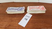 Two stacks of Canadian Tire money bills, one purple and one red, lying flat on a wooden surface next to a lot tag.