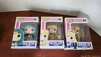 Three boxed Sailor Moon Funko Pop figures: Sailor Moon & Luna (#89) with box damage, Sailor Neptune (#298), and Sailor Venus & Artemis (#94).