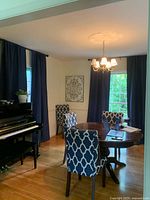 Photo showing two windows with navy blue rod top drapes, with the fabric hanging straight and evenly, displayed in a room with a chandelier and a piano.