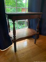 Full side view of the antique wooden table, showing spindle legs, under shelf, and lift-top with keyhole.