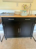Front view of butcher block kitchen cart showing two drawers, two-door cabinet and butcher block top with utensils and dishes
