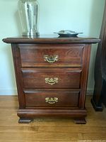 Full view of the Chippendale style solid wood bedside table showing three drawers and brass pulls.