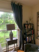 Dark gray drapes hanging on a window with grommet top, partially drawn and tied back, showing vertical folds and lining.